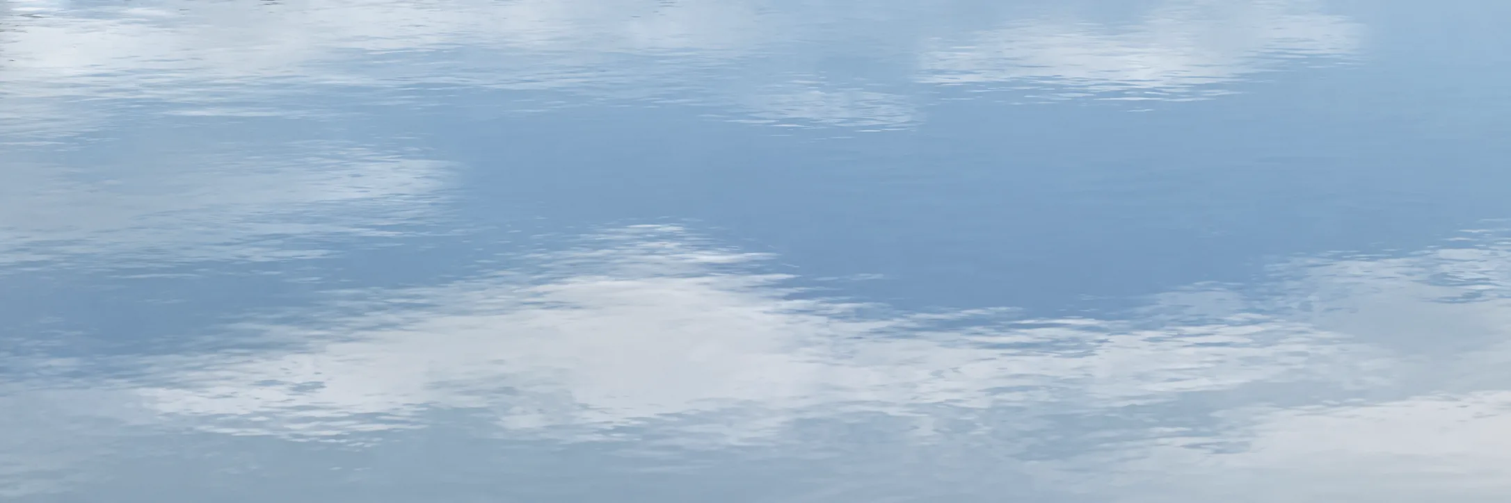 Close to still water, the sky and clouds lying on its surface