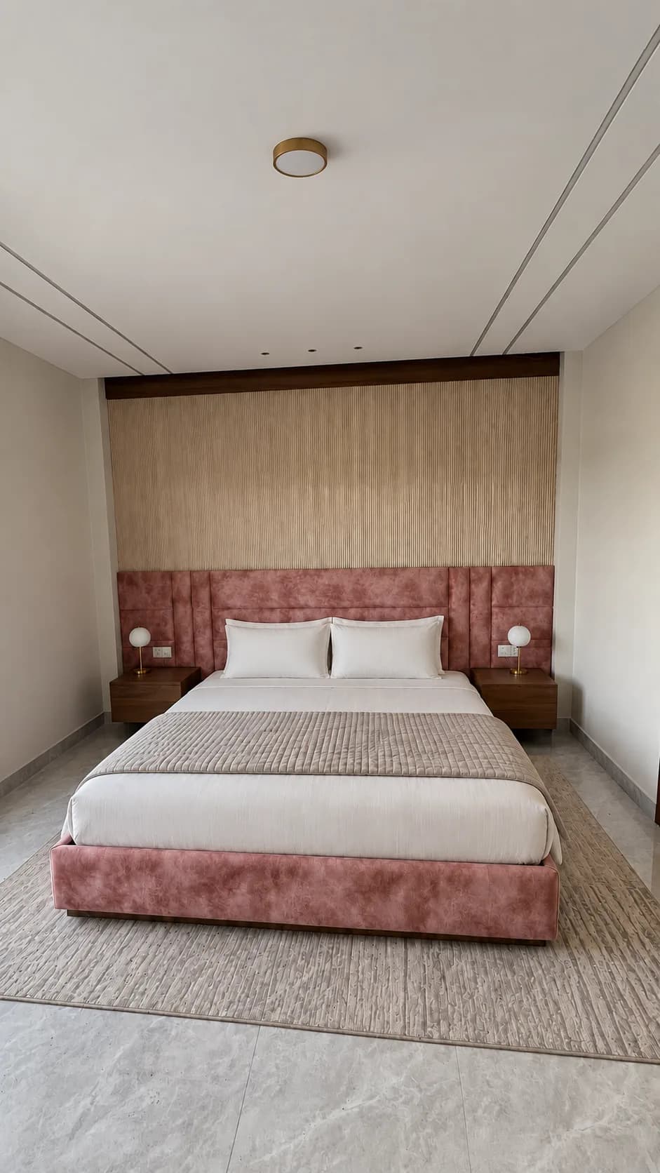 A villa bedroom: a bed with a rose-pink padded headboard, a rug and two bedside lamps