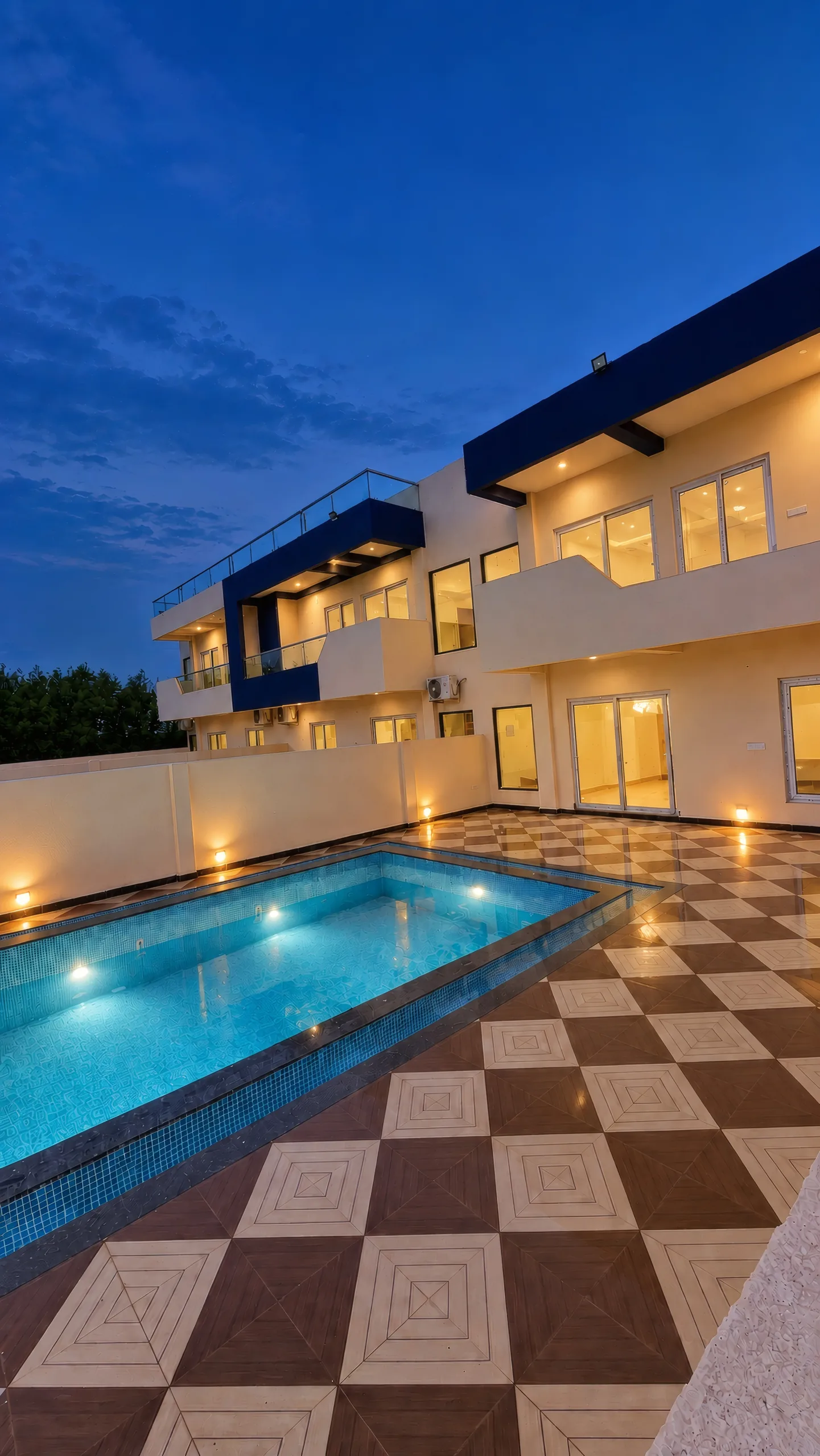 A villa courtyard at blue hour: the lit plunge pool, the checkerboard tiles and the two-storey villa with its navy-blue frame