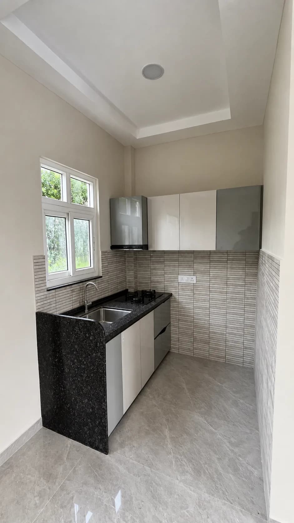 A villa's kitchen: a black granite counter under a window, tiled splashback and white cabinets