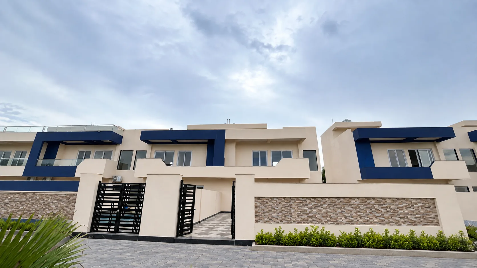 The villas seen from the road: two-storey fronts with navy-blue frames and black slatted gates, under a wide sky