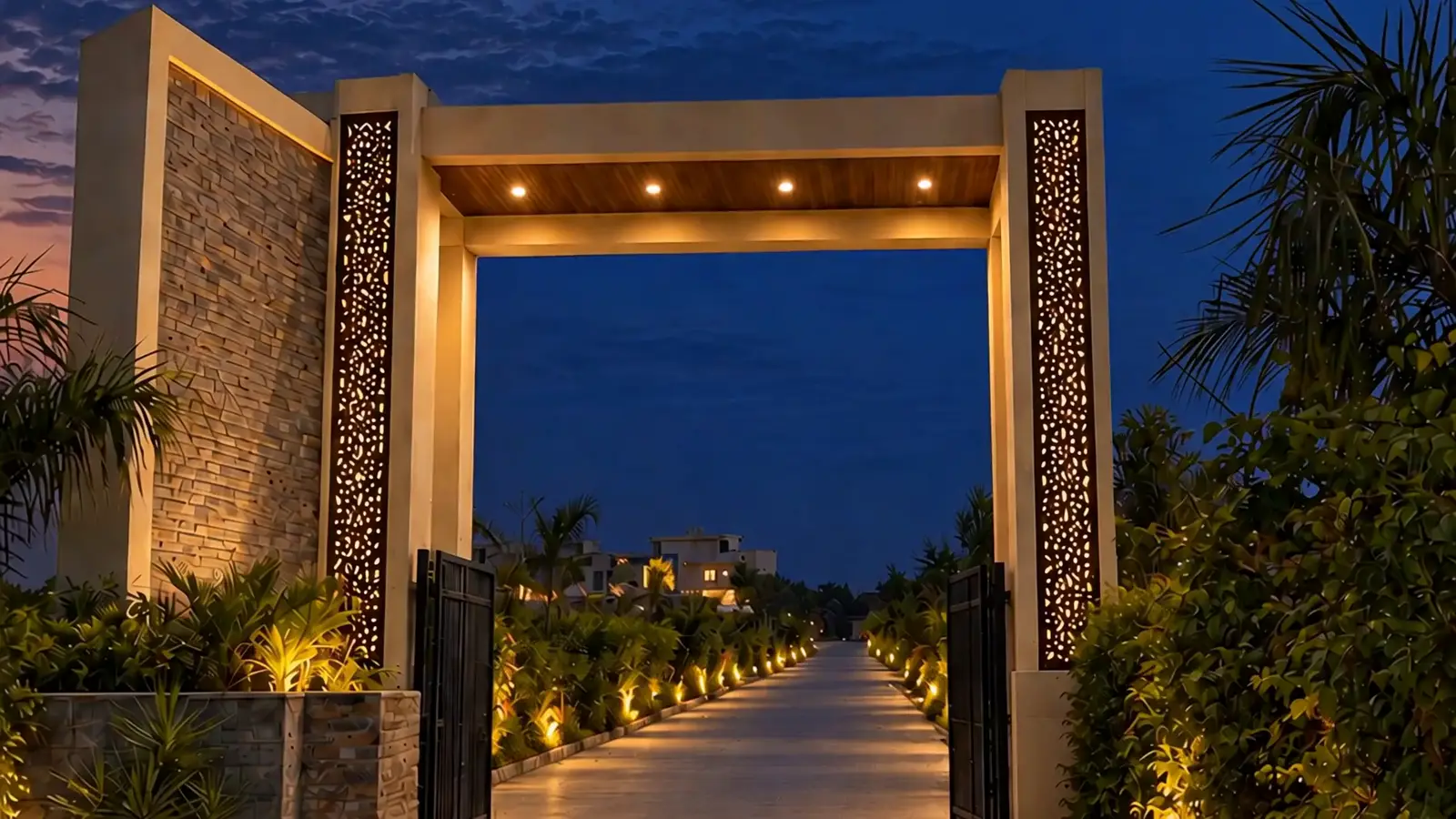 The entrance gate at blue hour, its jaali screens lit, the lamp-lined road running in