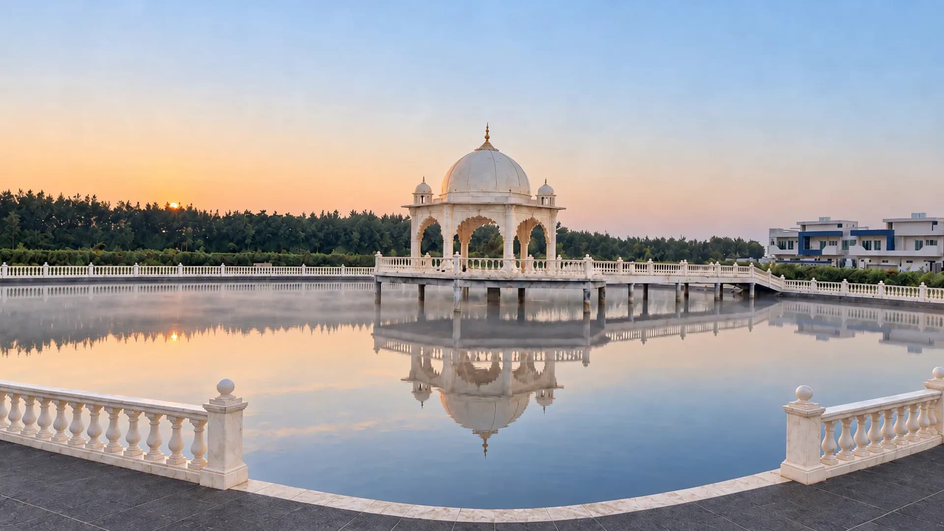 The white marble mandap on its stage in the pond, reached by a railed causeway, as the day turns to dusk
