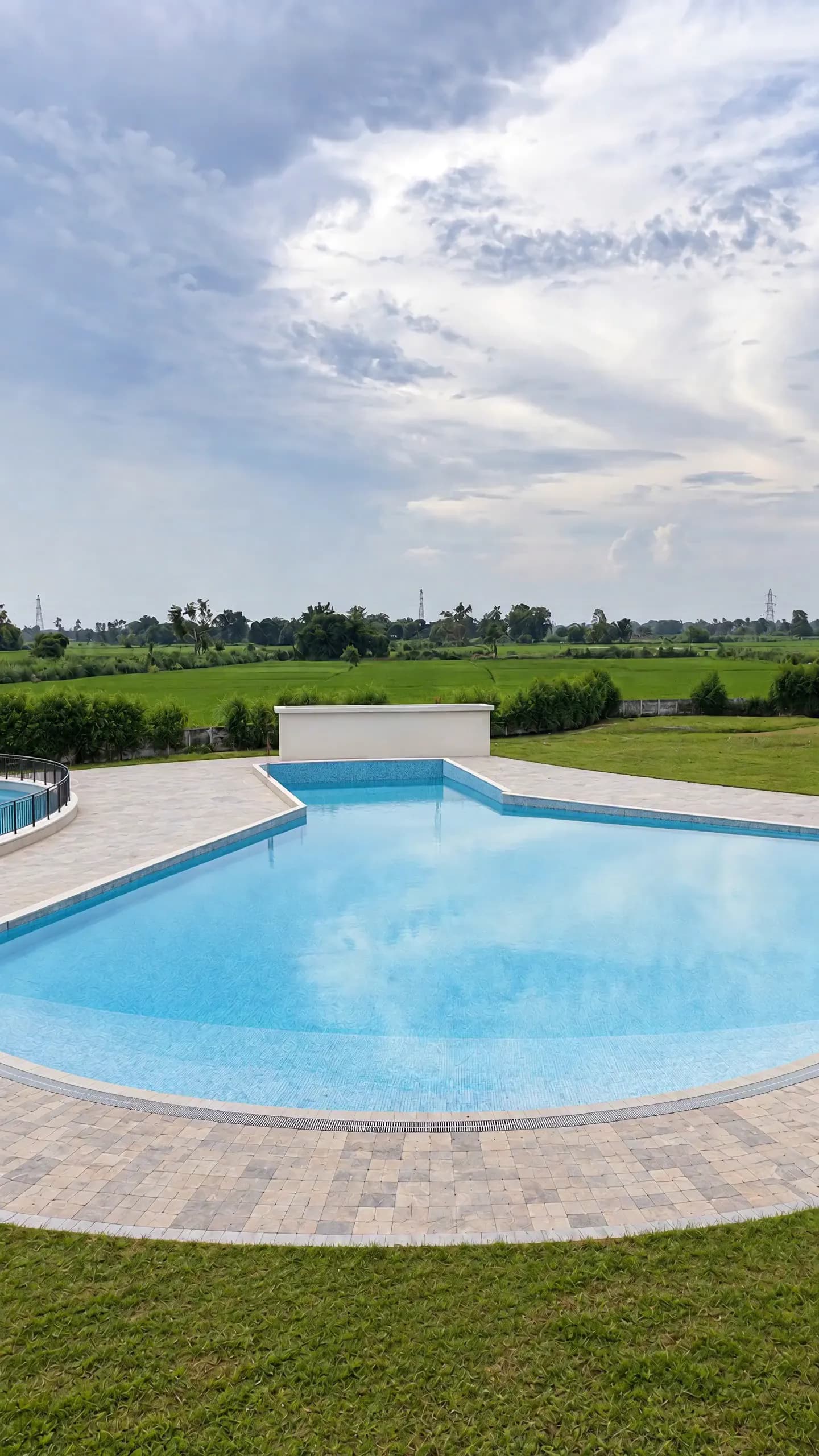 The wave pool under a big summer sky, its curved edge of pale stone set in the lawn