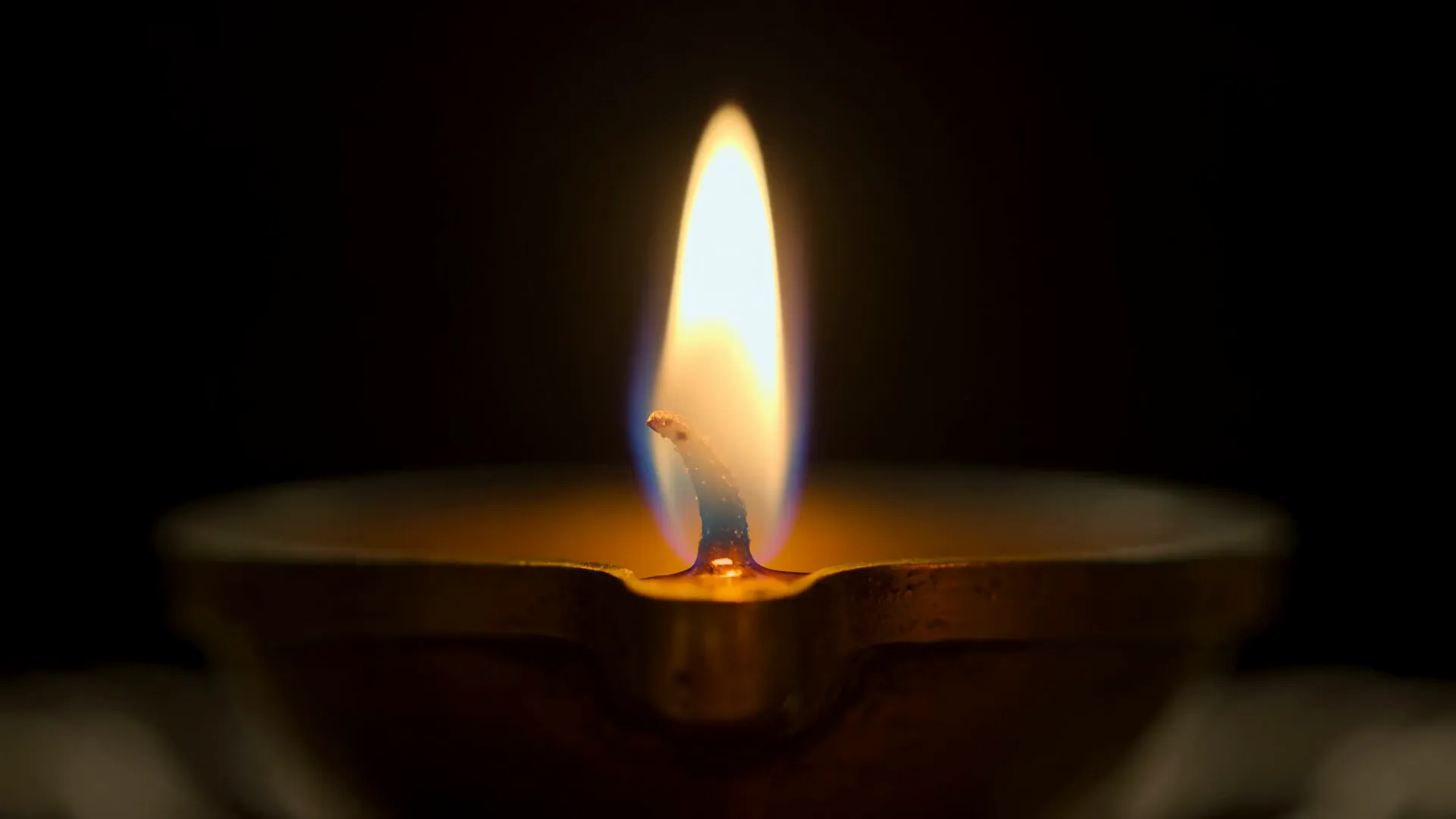 A single diya flame burning in the dark