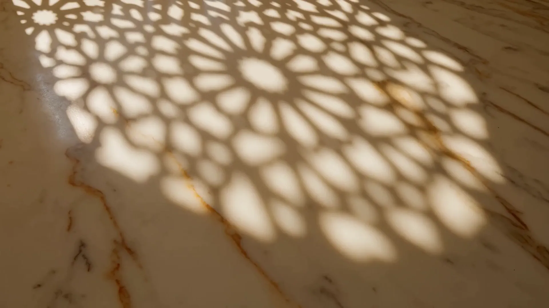 Light through a jaali screen moving slowly across warm marble