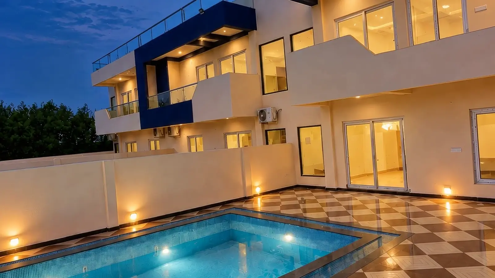 A villa courtyard at blue hour, the plunge pool lit and the rooms glowing