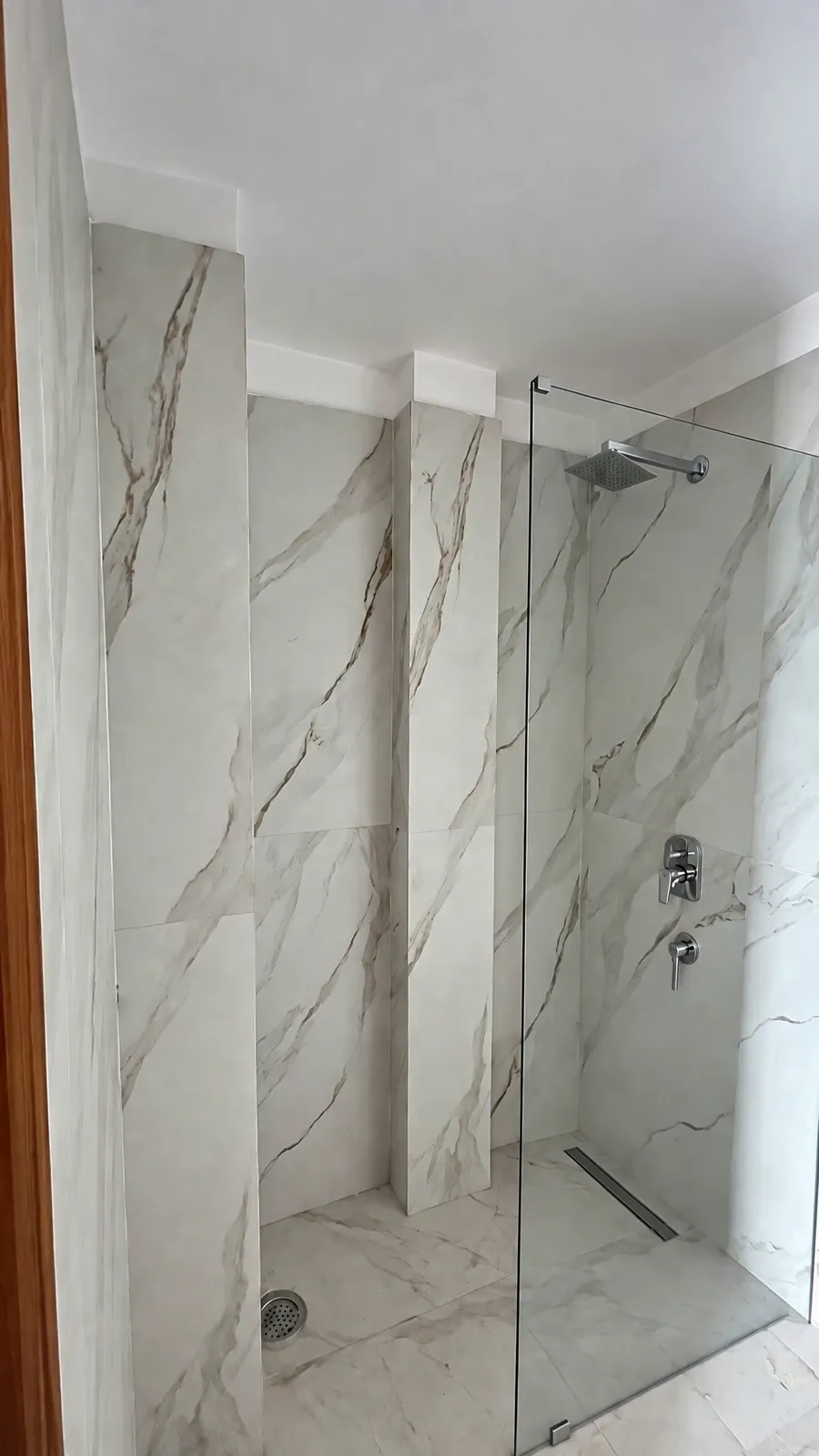A villa bathroom: a walk-in shower with white marble walls behind a glass screen