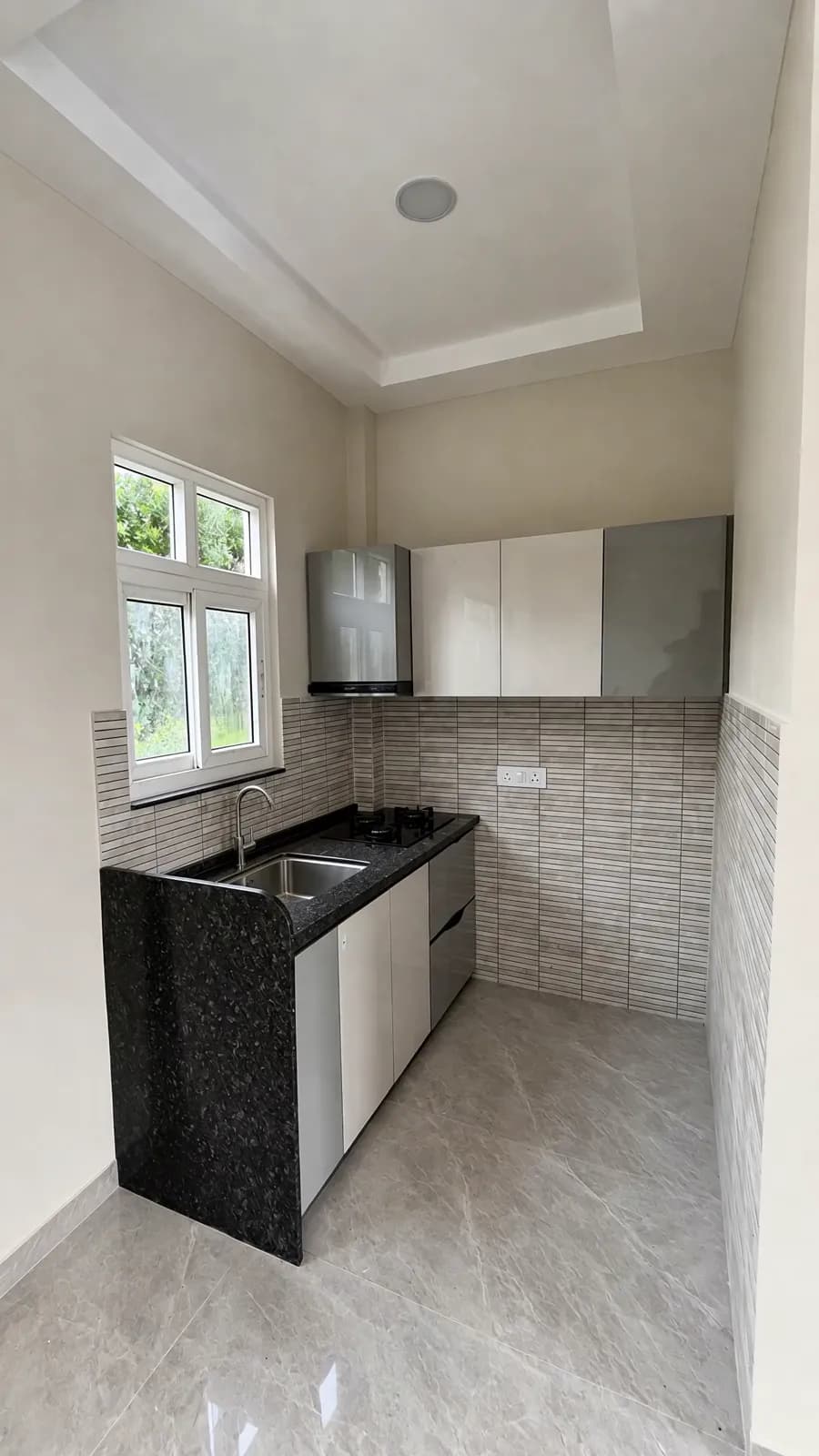 A villa's kitchen: a black granite counter under a window, tiled splashback and white cabinets